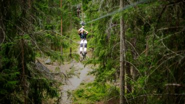 Kille kommer åkande längs en lång zipline genom skogen